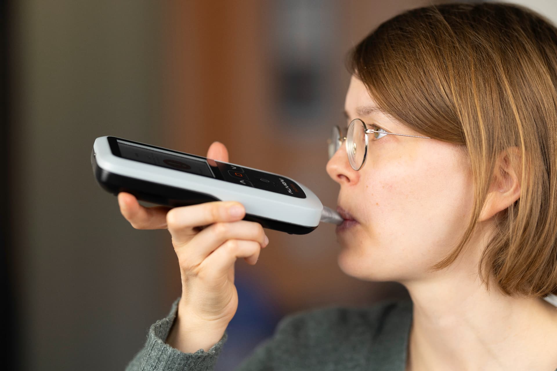 Person exhaling into the mouthpiece of a handheld Alivion breath-analysis device
